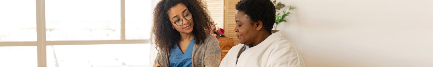 A middle-aged black woman receiving care at home from a young female care provider