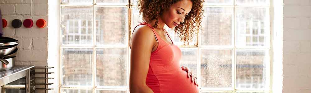 A young, 20-something African American mother-to-be with her hand resting on her pregnant belly